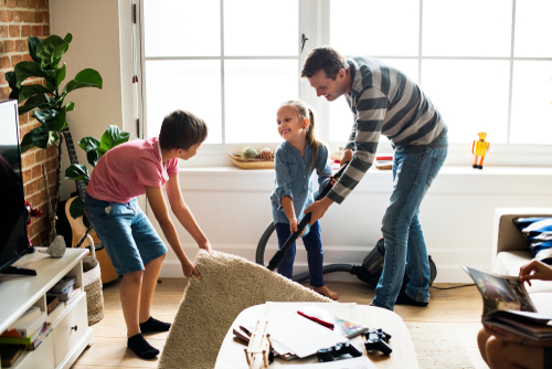 children helping a dad lifting carpet to clean hard wood floor in a living room